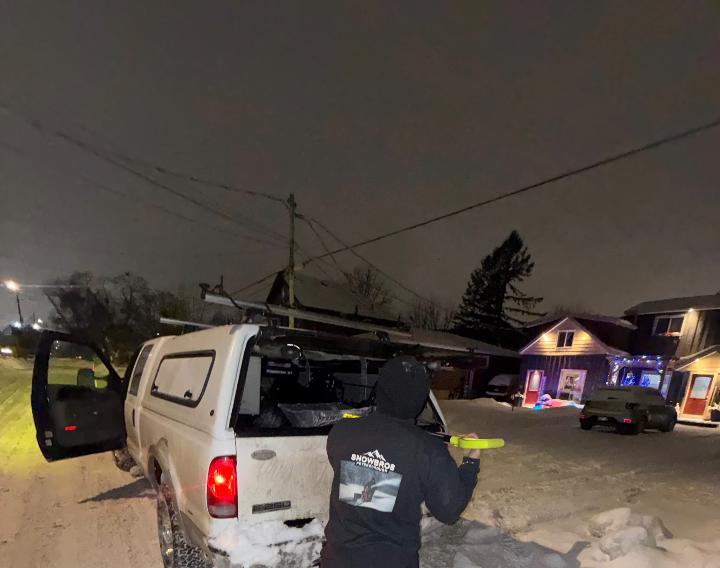 SnowBROS crew performing night-time snow clearing under residential streetlights